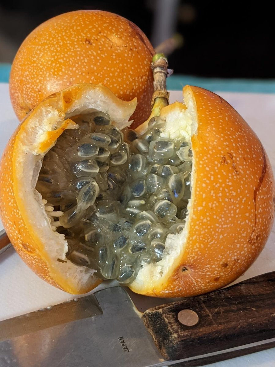 A granadilla cracked open on a cutting board revealing the sweet grey-green jelly and crunchy seeds