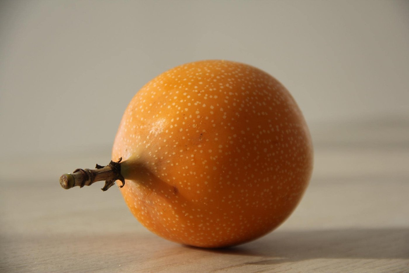 A single whole orange granadilla with its stem, skin flecked with tiny white speckles