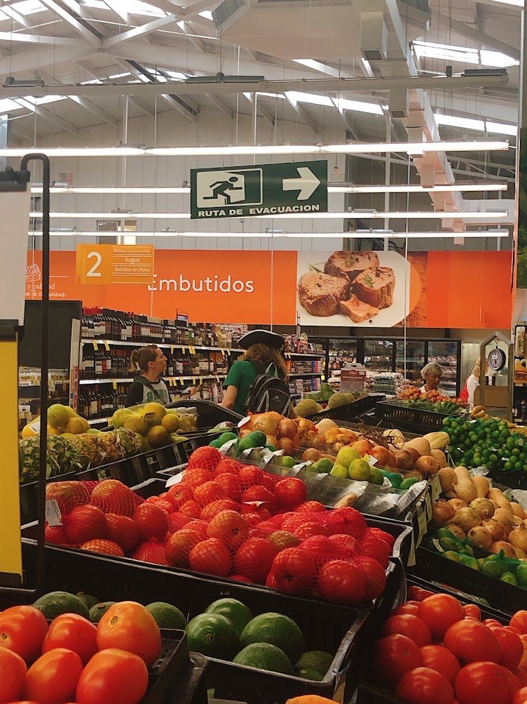 Fresh produce section at Más x Menos supermarket in Jacó — tomatoes, avocados, limes and onions