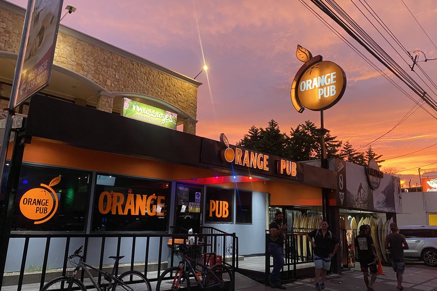 Orange Pub storefront lit up at sunset on Jacó's main strip