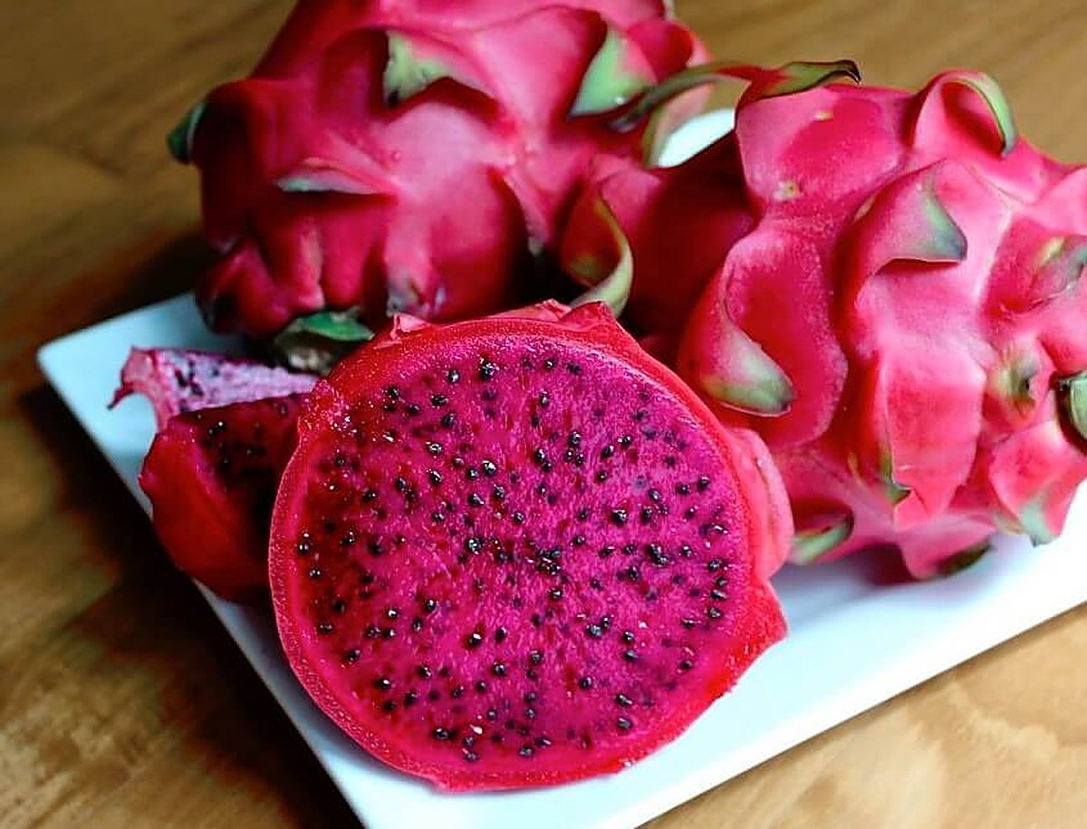 A dragon fruit sliced to reveal deep magenta-red flesh dotted with black seeds