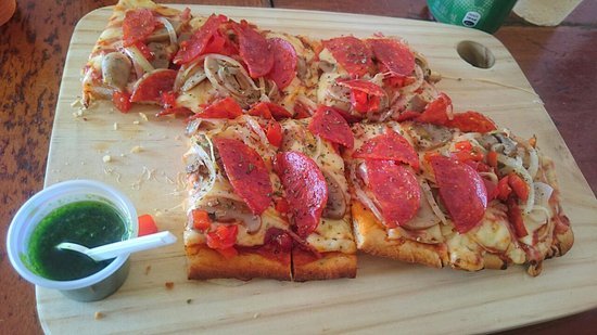 Pepperoni and vegetable pizza at Pizza Pata Jacó with a cup of homemade pesto