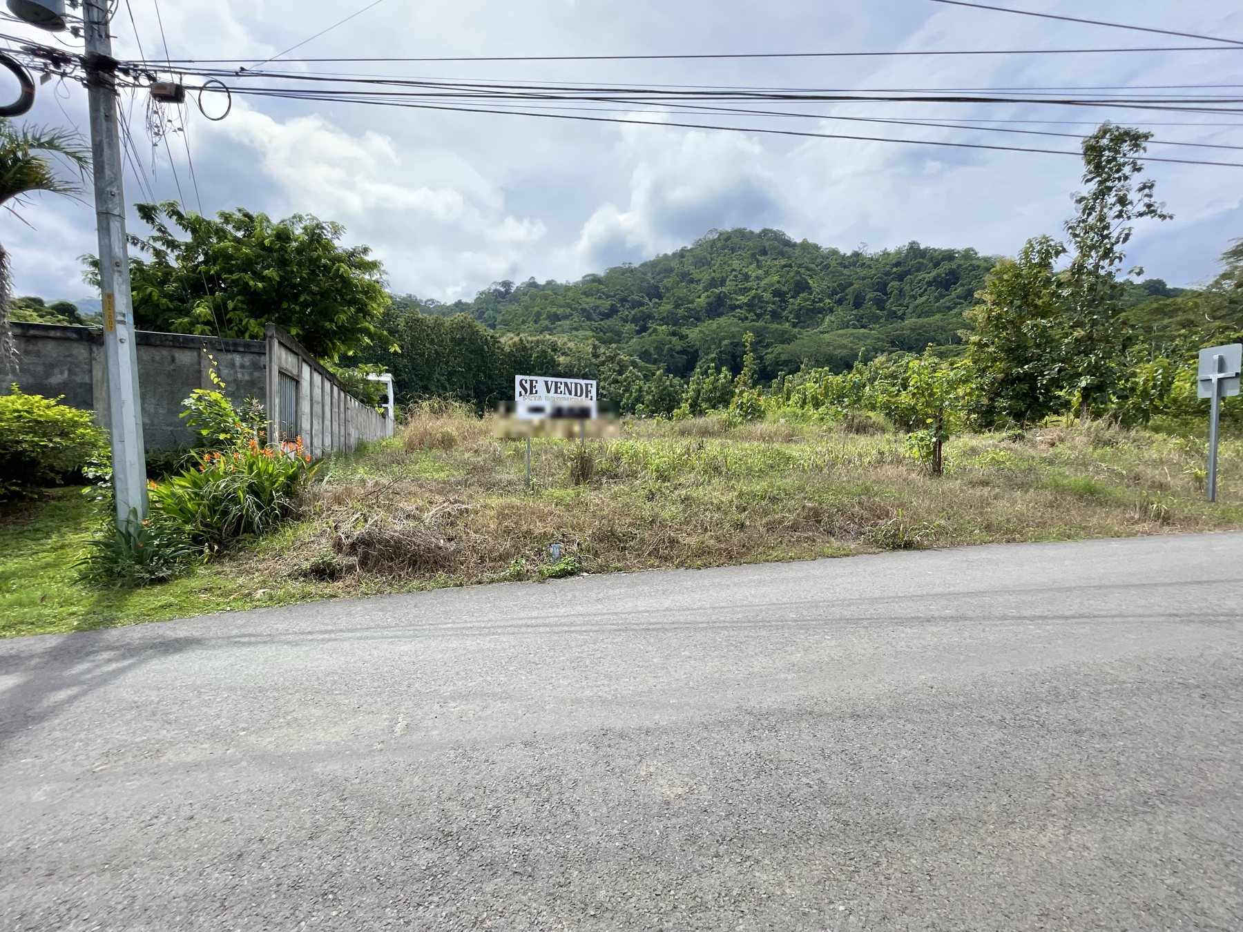 A cleared building lot for sale on a quiet paved road near Jaco Beach with a green mountain backdrop — best priced real estate near Jaco Beach, Costa Rica