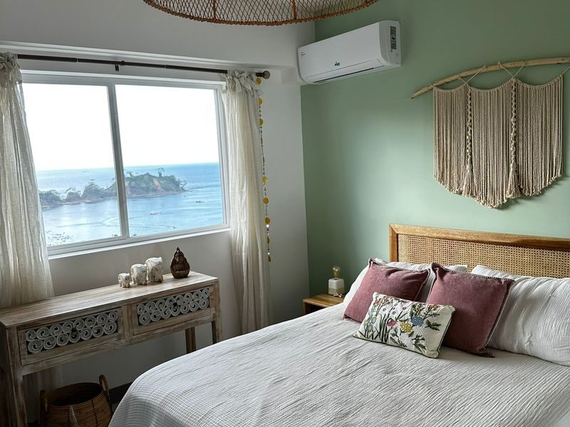 Master bedroom with direct ocean view window, split AC, and boho decor in the Playa Blanca apartment near Jaco