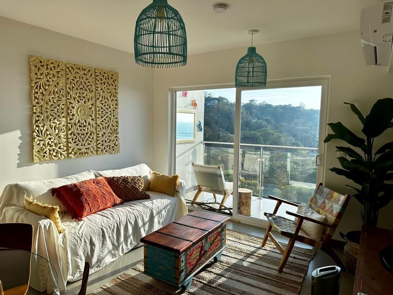 Bright living room with glass balcony doors overlooking ocean and mountains — Playa Blanca apartment for sale near Jaco Beach, Costa Rica