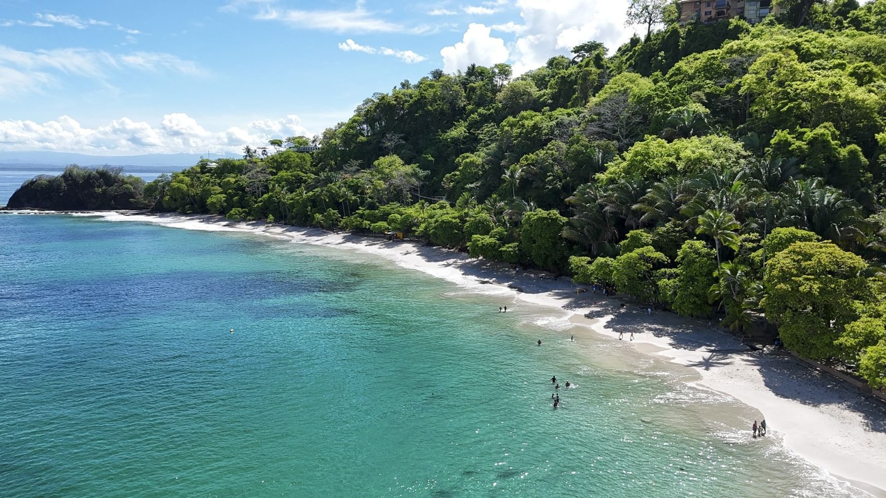 Forested point and swimmers on a white-sand beach at Punta Leona