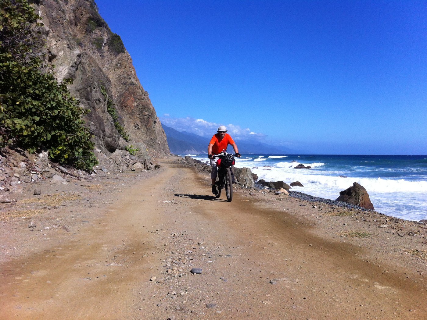 Cyclist riding along a black-sand beach beneath cliffs